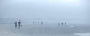 Plage panoramique dans un brouillard bleu dense. Plusieurs marcheurs avancent vers le photographe, dont un couple à gauche semblant discuter.