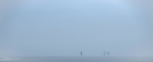Plage panoramique dans un brouillard bleu dense. Trois personnages apparaissent dans la moitié droite, une flaque de marée se trouve à l’extrême gauche.