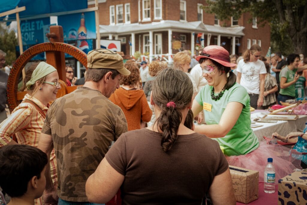 Sur le marché de Saint-Élie-de-Caxton, une vendeuse en t-shirt vert et chapeau rouge se détache parmi des visiteurs habillés de teintes brunes.