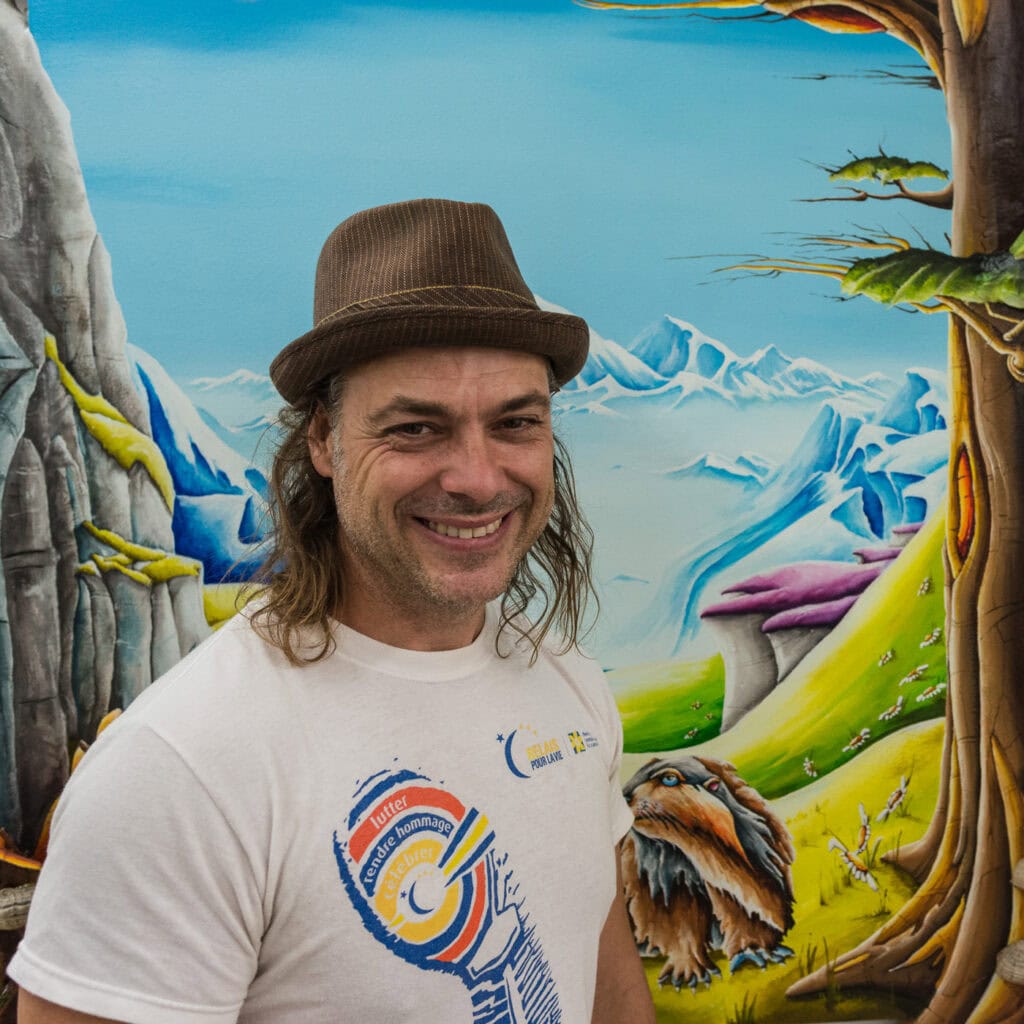 Jeune peintre souriant devant une œuvre colorée de style fantastique à Saint-Élie-de-Caxton.