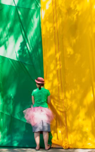 Jeune femme vue de dos devant deux grandes tentures verte et jaune, portant un chapeau rouge, un t-shirt vert et un tutu rose à Saint-Élie-de-Caxton.